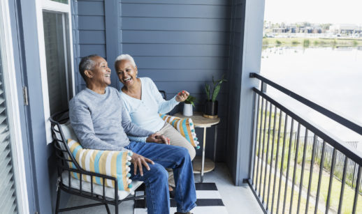 Um casal de idosos está feliz em uma varanda, em alusão ao momento da aposentadoria