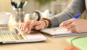 Pessoa usando escritório de contabilidade virtual, com a mão direita usando o laptop e a esquerda uma caneta