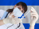Enfermeira com máscara segura seringa diante da bandeira de Israel