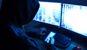 Hacker tentando invadir sistemas com duas telas de computador
