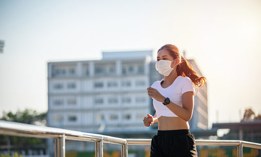 Mulher asiática correndo na rua com máscara de proteção