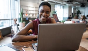 Mulher negra sorrindo em frente ao computador em mesa de escritório