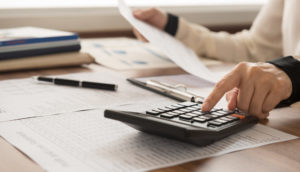 Pessoa com calculadora, papéis e canetas cuidando de finanças pessoais