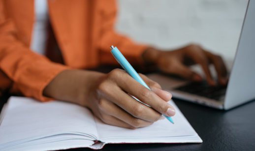 Mãos de mulher digitando em laptop e fazendo anotações sobre sua saúde financeira em um caderno