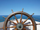 Safra Report: roda de leme de barco em alto mar, com céu e mar azuis calmos