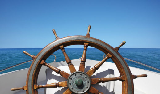 Safra Report: roda de leme de barco em alto mar, com céu e mar azuis calmos