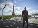Michael Jordan de pé com terno, seu tênis, em quadra de basquete com fundo para a Torre Eiffel