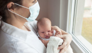 bebê no colo de mãe com máscara anti-covid