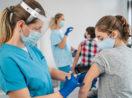 Enfermeira aplicando vacina da Pfizer em menina adolescentes, ambas de máscara