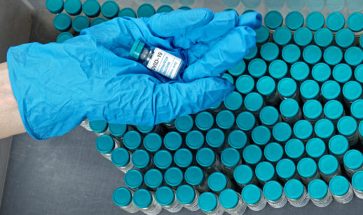 Mãos com luvas segurança dose da vacina contra covid-19 sobre dezenas de frascos