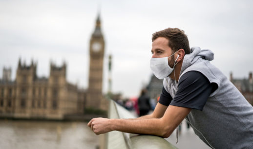 Homem de colete, camiseta e máscara em ponte em frente ao relógio do Big Ben, em Londres