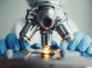 Mãos de cientista manipulando placa de baixo de telescópio em laboratório de biotecnologia