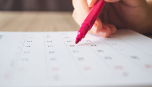 Mão de pessoa com com caneta rosa escrevendo em agenda semanal
