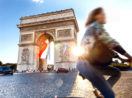 Mulher passeando de bicicleta com o Arco do Triunfo ao fundo, em Paris, na França