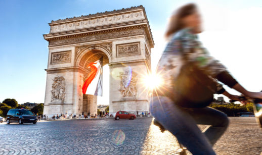 Mulher passeando de bicicleta com o Arco do Triunfo ao fundo, em Paris, na França