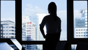 Mulher olhando o horizonte por janela pensando na conjuntura Safra Invest