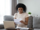 Mulher segurando recibos e notas para deduções no imposto de renda em frente ao computador