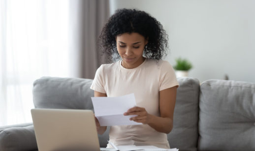 Mulher segurando recibos e notas para deduções no imposto de renda em frente ao computador