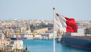 Foto da bandeira de Malta com paisagem da ilha ao fundo