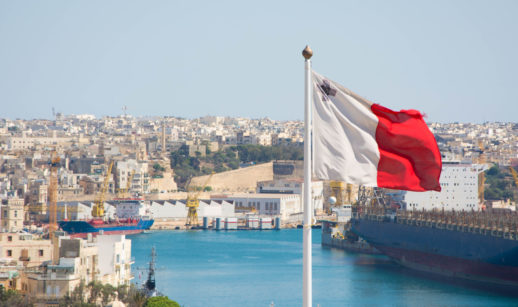 Foto da bandeira de Malta com paisagem da ilha ao fundo