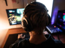 Pessoa de costas com fone de ouvido e duas telas de jogo de computador, tema da Tech Thursday