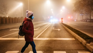 Pessoa atravessa rua no frio, de gorro e máscara