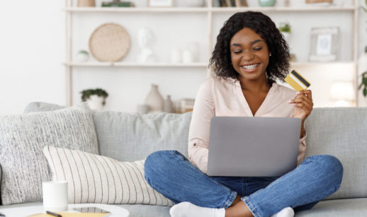Mulher feliz sentada no sofá com laptop e cartão de crédito em mãos comprando na Prime Day da Amazon