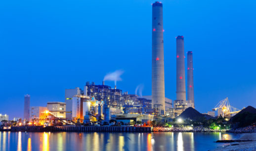 Foto de fábrica no início da noite com chaminés em destaque, em alusão às emissões e créditos de carbono