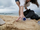 Pessoa recolhendo garrafa de plástico de areia em praia