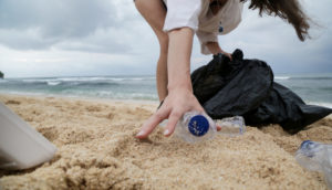 Pessoa recolhendo garrafa de plástico de areia em praia