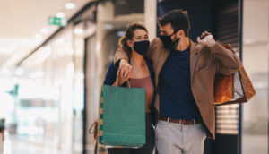 Casal com máscaras e sacola de compras em shopping, alusivo à confiança do consumidor