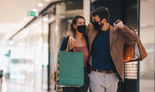Casal com máscaras e sacola de compras em shopping, alusivo à confiança do consumidor
