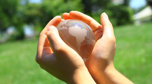 Mãos segurando um globo de vidro com destaque para a América do Sul em meio à natureza de fundo, alusivo aos conceitos ESG