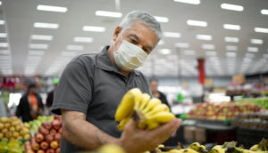 Pessoa de máscara pegando cacho de banana no mercado