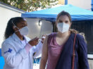 Enfermeira aplicando dose no braço de jovem a ser vacinado no Brasil