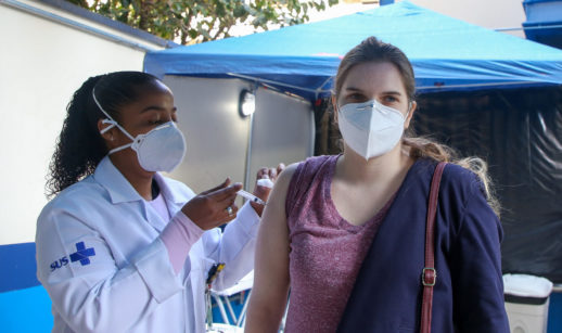 Enfermeira aplicando dose no braço de jovem a ser vacinado no Brasil