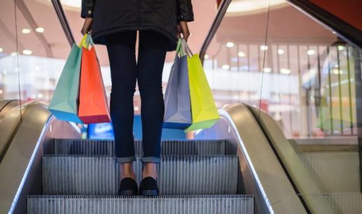 Pessoa subindo escada rolando com sacolas nas mãos em shopping, alusivo às ações da Multiplan