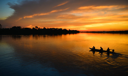 Barco com pessoas em crepúsculo no rio na região da Amazônia, onde serviço de internet será disponibilizado