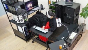 Mulher deitada no colchão gamer da Bauhütte com mesa, telas de computador e pequenos armários