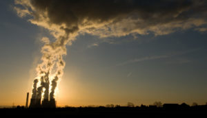 Paisagem do pôr do sol com destaque para chaminé de fábrica soltando fumaça, alusivo às emissões de metano