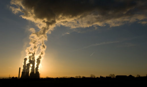 Paisagem do pôr do sol com destaque para chaminé de fábrica soltando fumaça, alusivo às emissões de metano