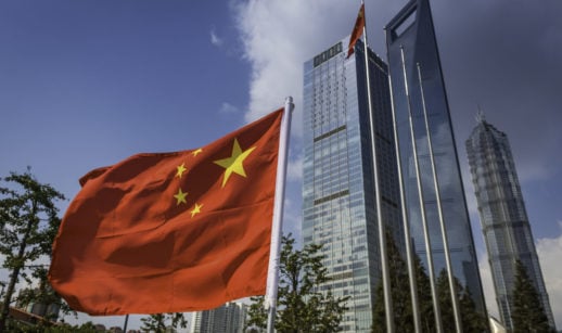 Bandeira da China em primeiro plano com prédios espelhados atrás, alusivo à incorporadora Evergrande e sua venda de fatia em banco
