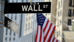 Placa de Wall Street com bandeiras dos EUA ao fundo em Nova York, onde há uma sede do Federal Reserve