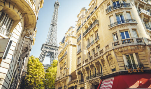Perspectiva de baixo para cima de prédios históricos de Paris, com destaque para a palavra "café" e a Torre Eiffel ao fundo, alusivo ao passaporte da vacina exigido na França