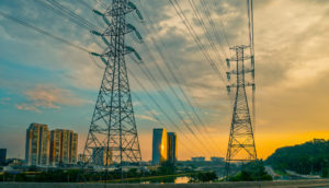 Torres de transmissão de energia sobre ponte e ao lado do Rio Pinheiros com pôr do sol ao fundo, em São Paulo, alusivo ao leilão emergencial