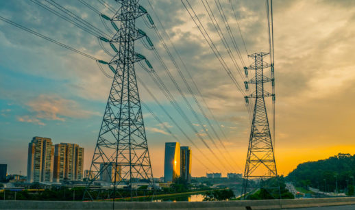 Torres de transmissão de energia sobre ponte e ao lado do Rio Pinheiros com pôr do sol ao fundo, em São Paulo, alusivo ao leilão emergencial