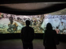 Duas pessoas de costas observando tela da exposição "O Dia Seguinte", sobre mudanças climáticas