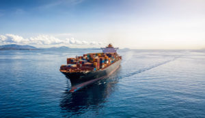 Navio cargueiro com muitos contêineres em meio ao mar azul, alusivo ao transporte sustentável pretendido por Amazon e outras gigantes