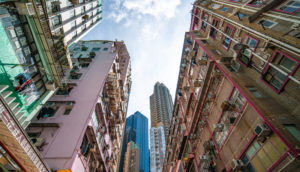 Perspectiva de baixo para cima de prédios residenciais pobres na China e, ao fundo, prédios modernos comerciais, alusivo às desigualdades do país