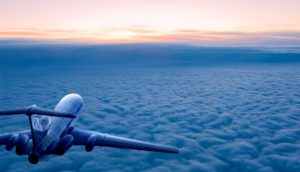 Paisagem aérea de avião à esquerda sobrevoando nuvens em meio as nascer do sol, alusivo ao combustível para aviação sustentável